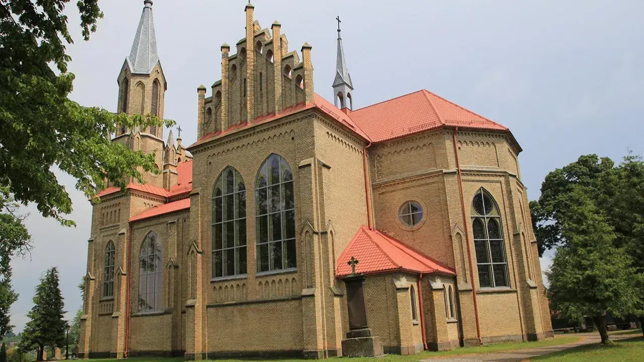 Gotycka ceglana świątynia z czerwonym dachem, jedna z krynki atrakcje. Wokół drzewa i trawnik.